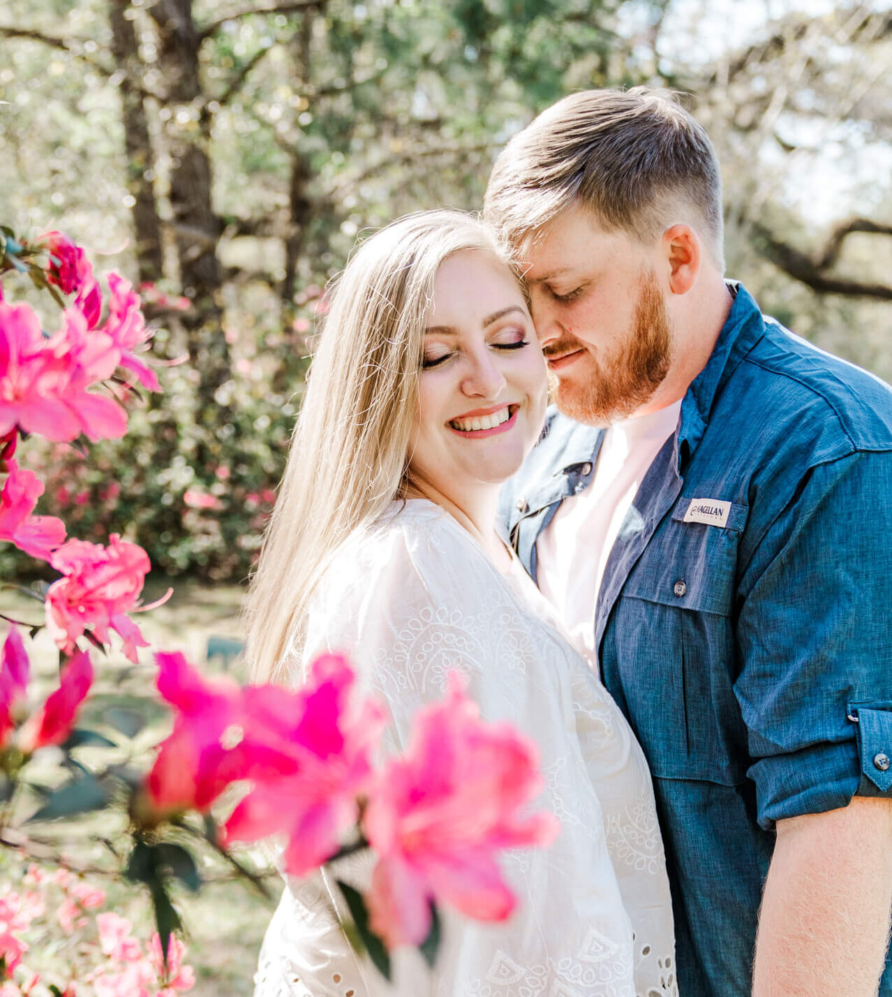 Man and woman stand snuggled up with eyes closed near blooming azalea bush for their Blakeley State Park engagement photos
