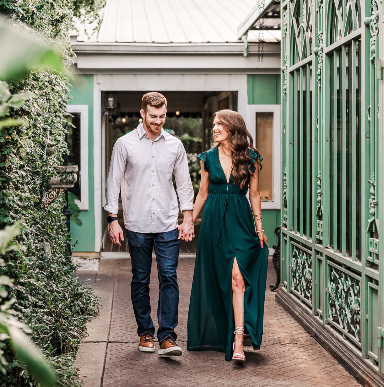 Man and woman walking through path in downtown Fairhope's French Quarter for their engagement photos. They are laughing and smiling while holding hands.