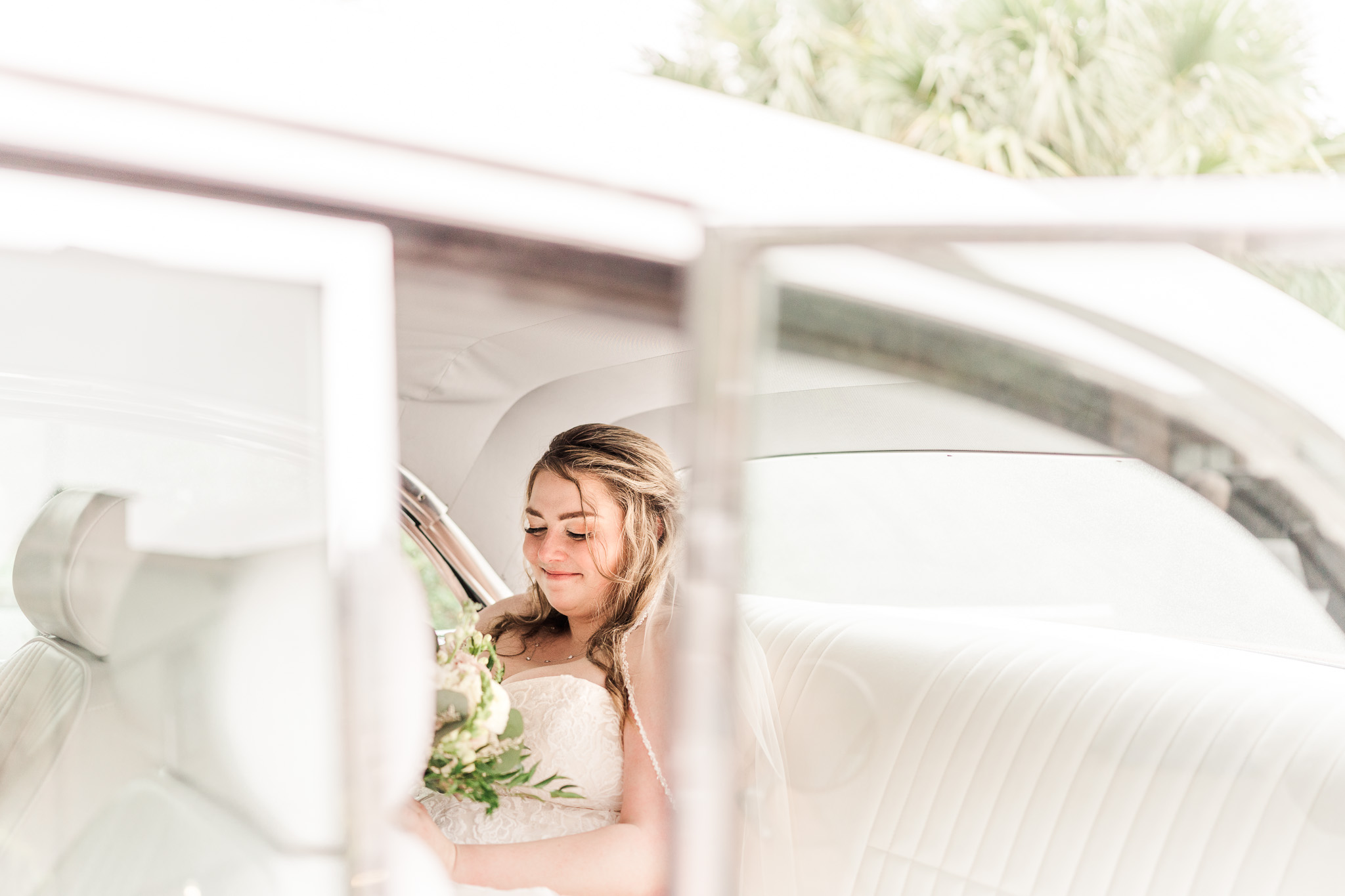 Bride looks down at her bouquet of flowers and waits for her groom while sitting in a vintage Chevy car for their Fairhope wedding video.