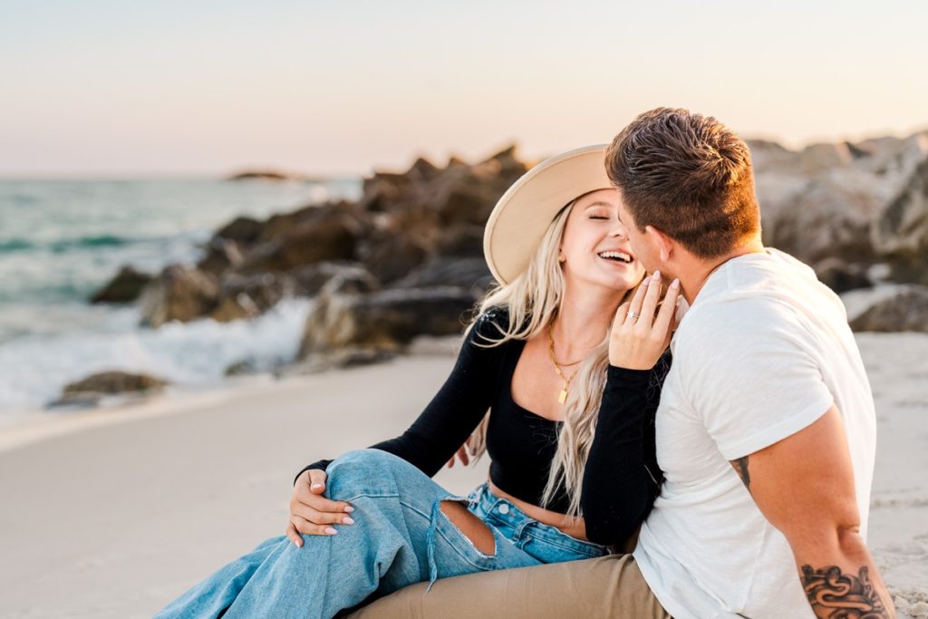 Engaged couple sitting in the sand and laughing at Alabama Point in Orange Beach, AL for their beach engagement photos