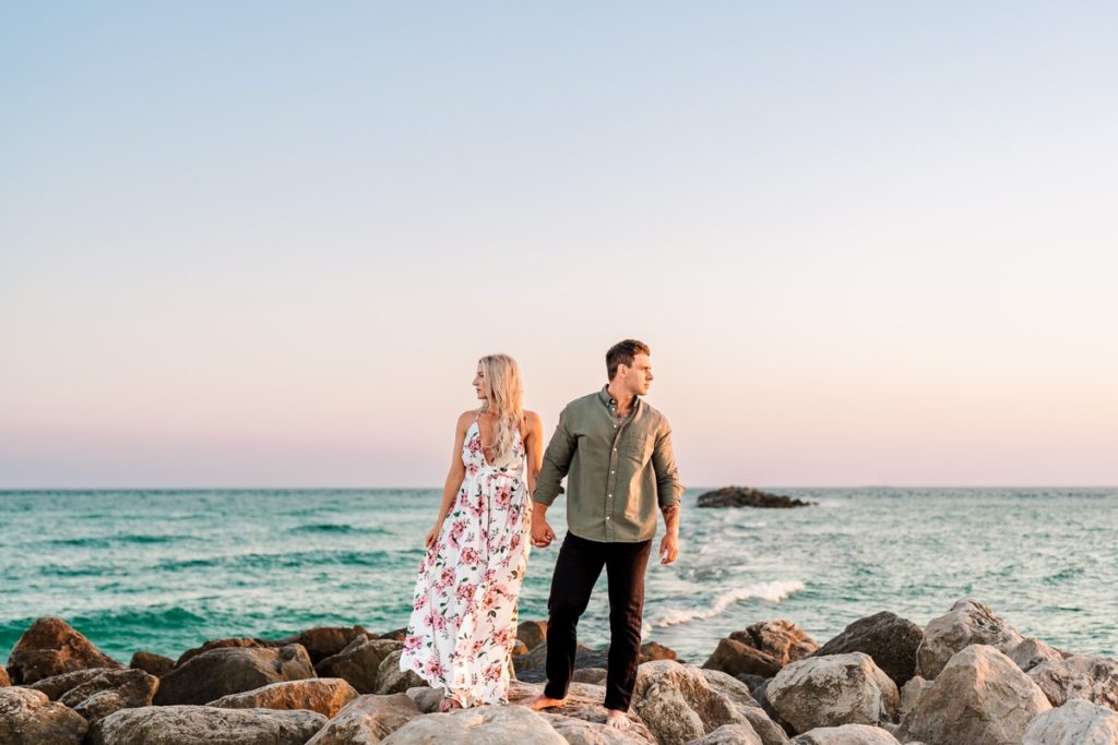 Engaged couple standing on jetty rocks and looking in the distance at Alabama Point in Orange Beach, AL for their beach engagement photos