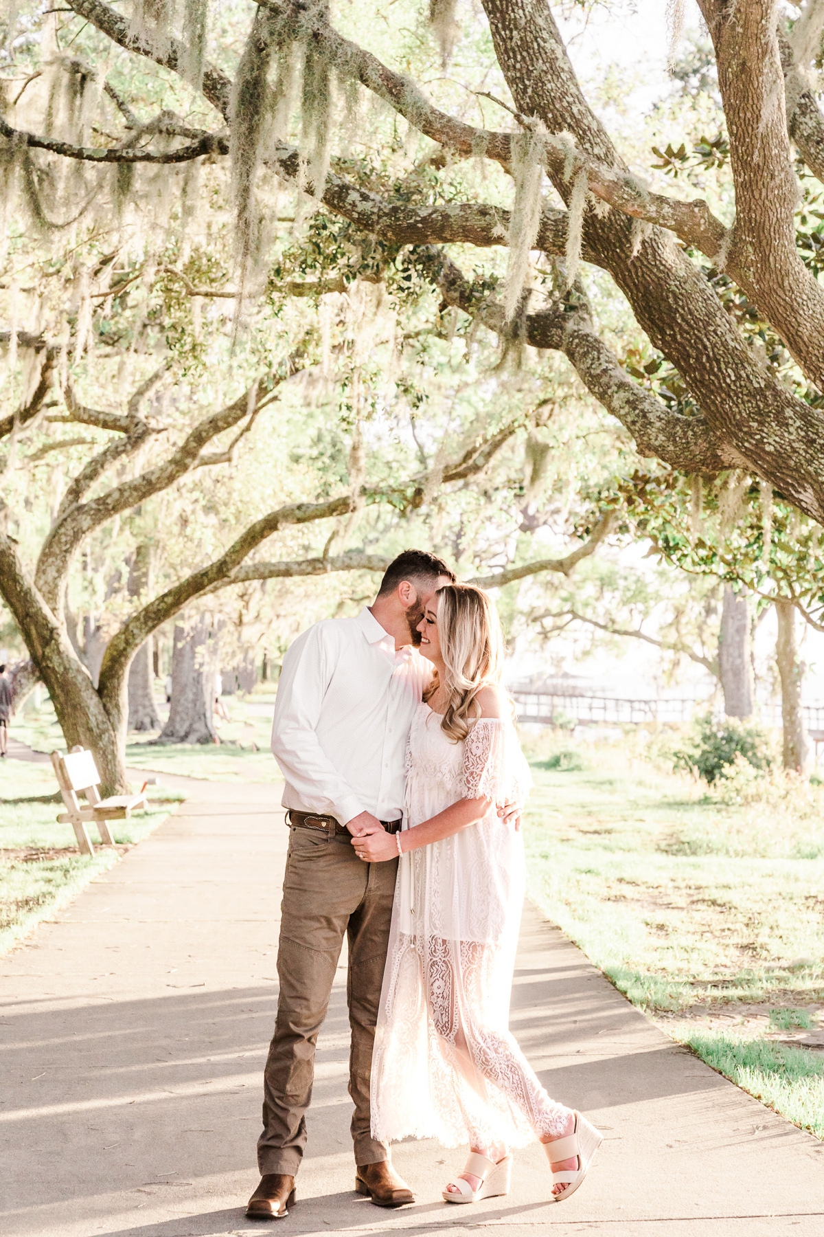 Husband- and wife-to-be take a walk along an oak tree covered path at the Fairhope, AL Bluffs for their Downtown Fairhope engagement photos
