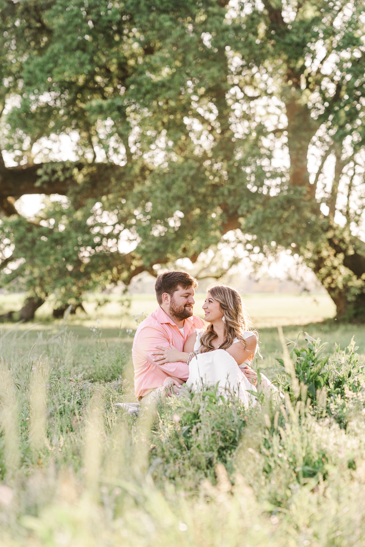 Man and woman sit down in a field snuggled close for their Oak Hollow Farm engagement photos.