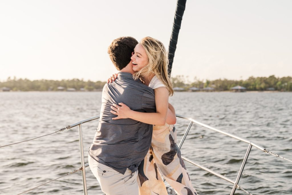 Man gets down on one knee and proposes to girlfriend on Orange Beach Sailboat tour and woman is overcome with joy, smiling big