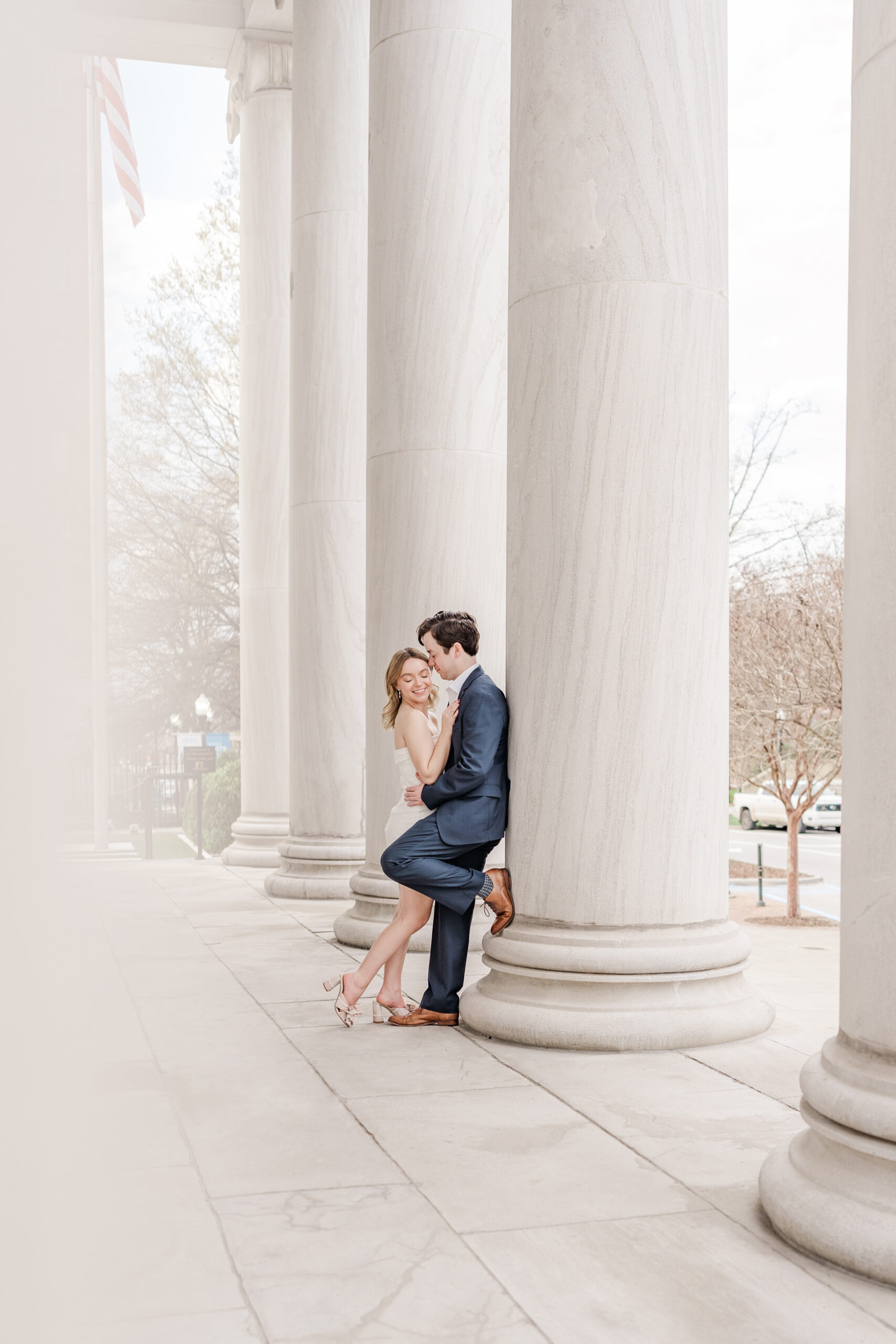 Bride- and groom-to-be snuggle up on a column at the First National Bank for their downtown Huntsville engagement photos