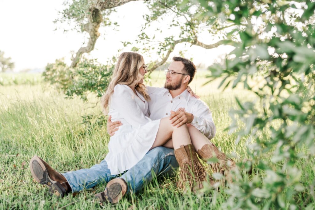 Man and woman snuggle up under a tree for their Fairhope engagement photos at Oak Hollow Farm