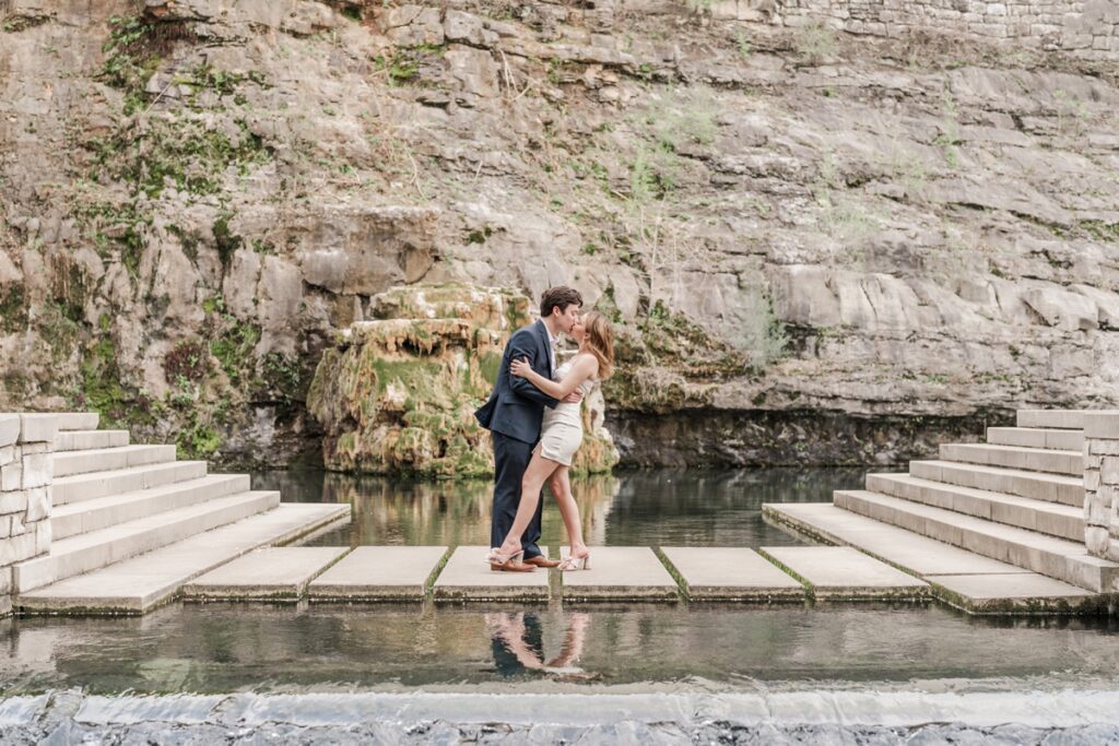 Bride- and groom-to-be dip and kiss on a stone bridge in Big Spring Park for their downtown Huntsville engagement photos