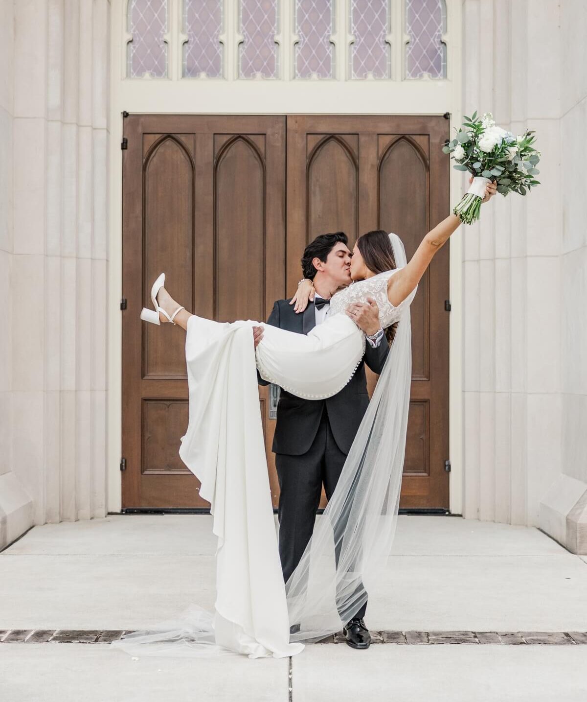 Groom lifts up bride while they kiss and she holds up her bouquet in the air for their St. Ignatius Catholic Parish Church and Bragg-Mitchell wedding photos and video