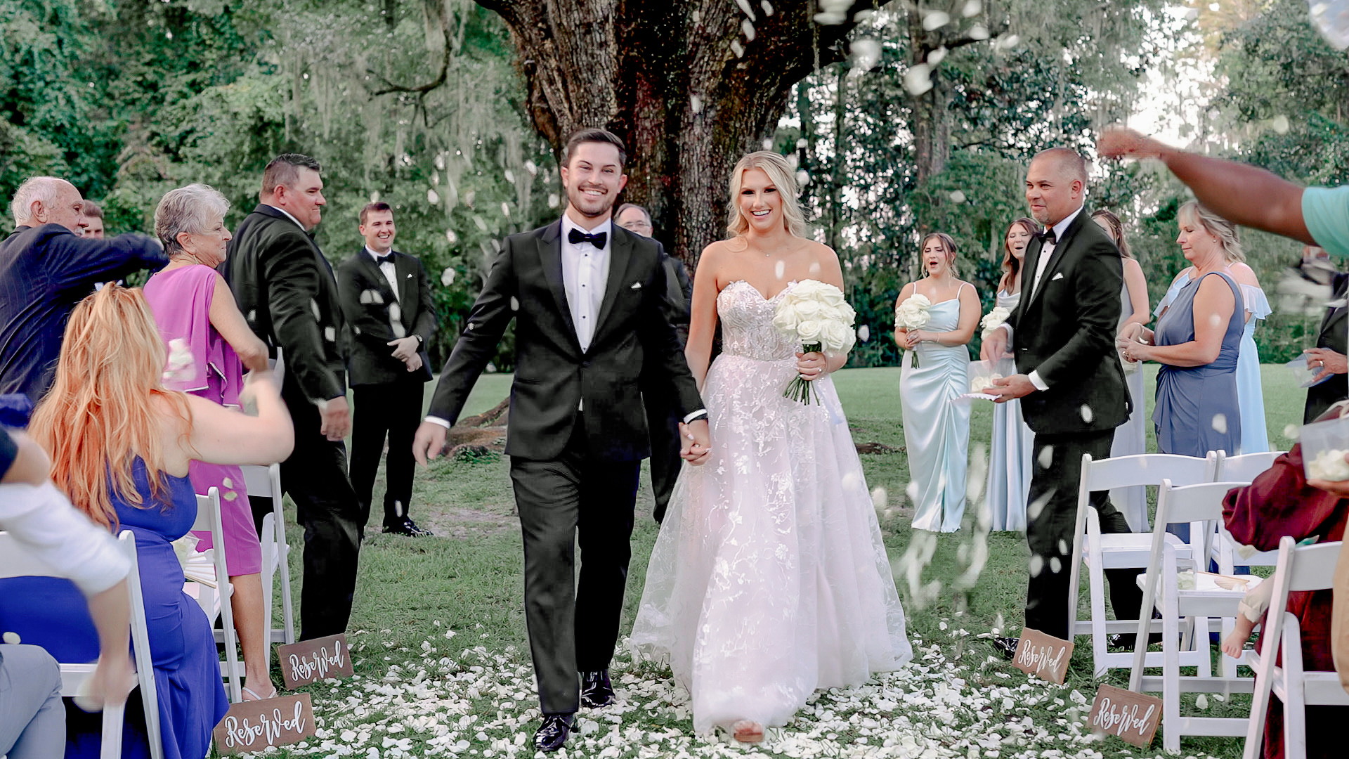 Bride and Groom walk down ceremony aisle while their guests toss flower petals above them