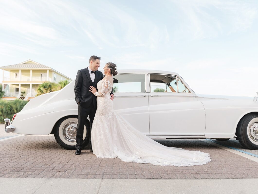 Bride and groom stand face-to-face in front of white vintage Rolls-Royce