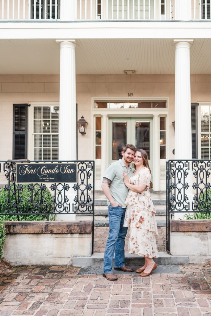 Man and woman pose in front of wedding venue for their Fort Conde Inn engagement photos in Mobile, Alabama