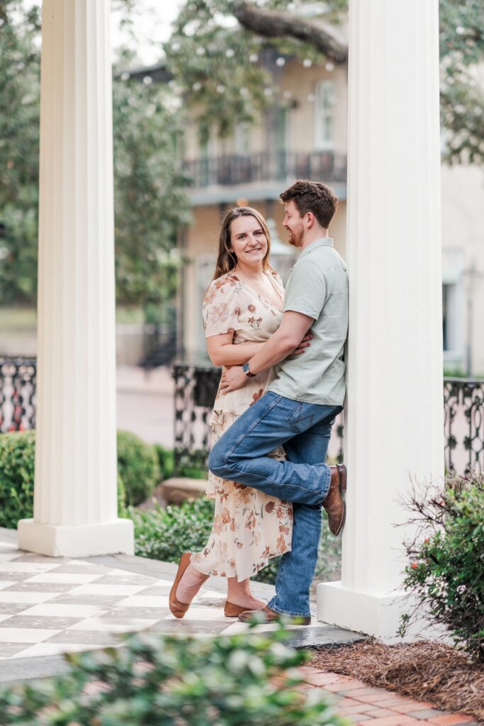 Man and woman lean against column at the historical Fort Conde Inn in Mobile, AL for their engagement photos