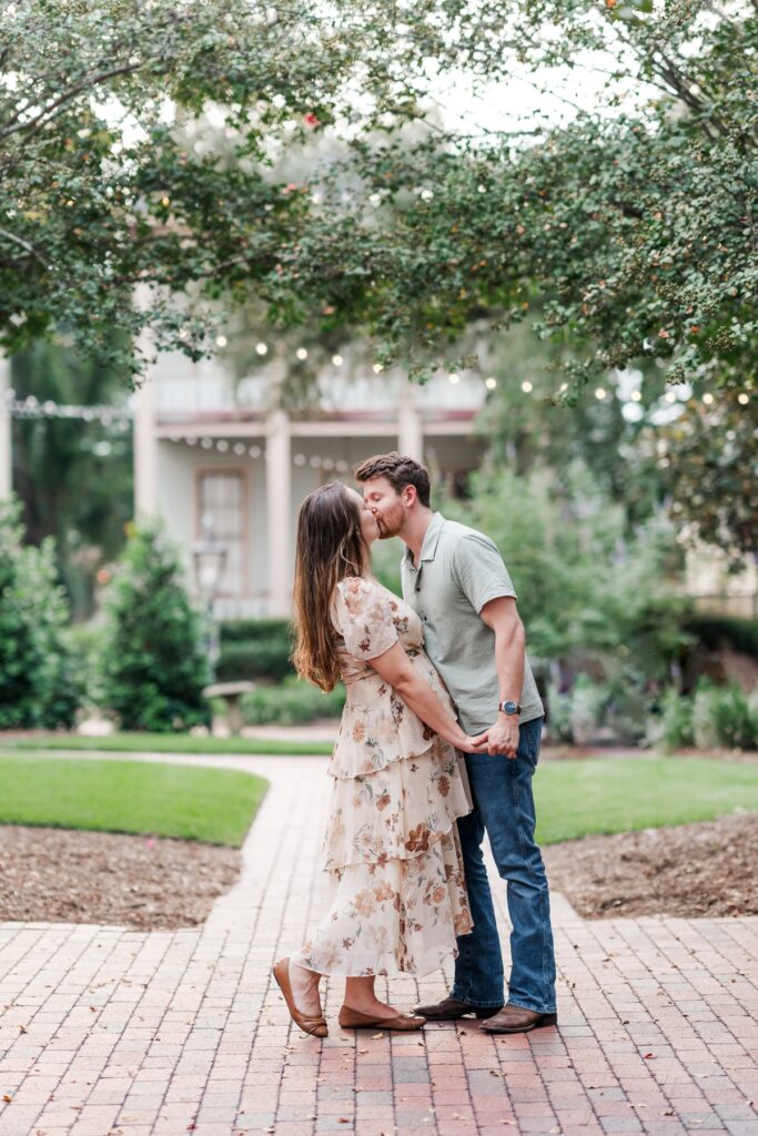 Man and woman kiss on path at the historical Fort Conde Inn in Mobile, AL for their engagement photos