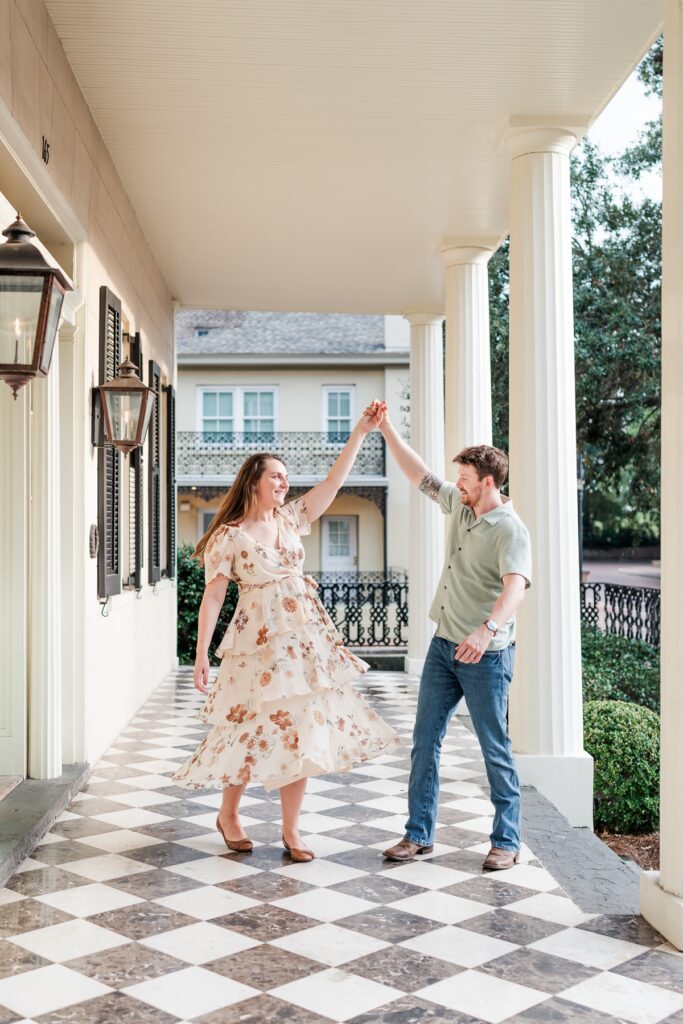 Man twirls woman on the front porch at the historical Fort Conde Inn in Mobile, AL for their engagement photos