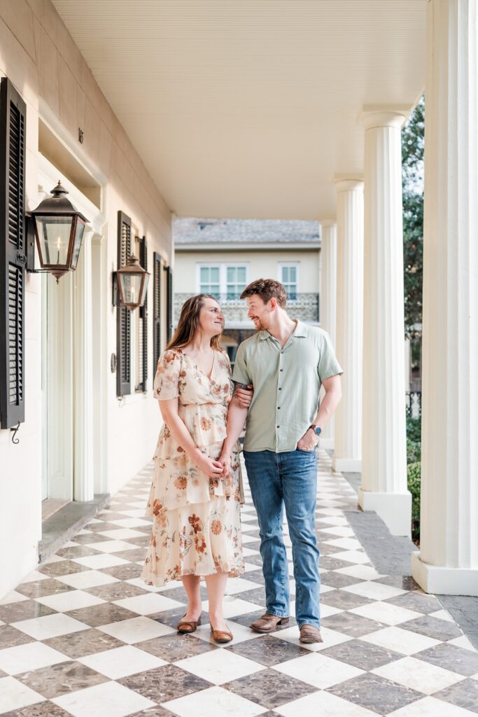 Man walks with woman on the front porch at the historical Fort Conde Inn in Mobile, AL for their engagement photos