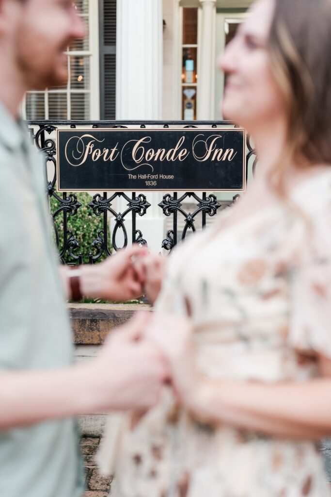Man and woman stand in front of venue sign at the historical Fort Conde Inn in Mobile, AL for their engagement photos